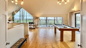 Una habitación amplia con mesa de billar, ventanas grandes y suelo de madera.