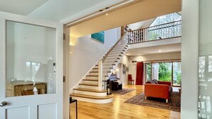 Un amplio salón con una escalera de madera, un piano y un sofá rojo.