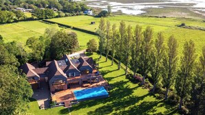 Una casa grande con piscina, rodeada de campos verdes y árboles.