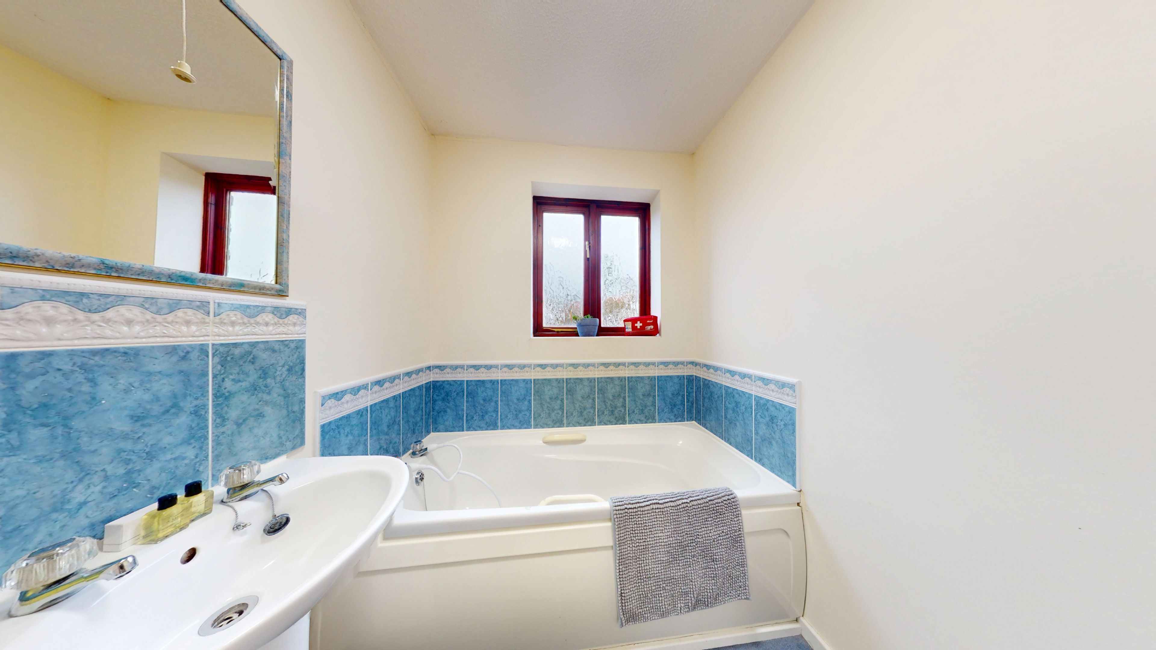 A bathroom with a bathtub, a sink, and a window with a red curtain.