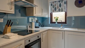 A modern kitchen with white cabinets, a black countertop, and a window with patterned curtains. - Spires View | Oxford Holiday Let | 1 Bed & Sleeps 2 (Oxford)