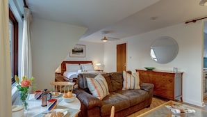 A cozy living room with a brown leather sofa, a wooden coffee table, and a dining area with a white table and chairs. There is a wooden cabinet and a mirror on the wall. - Spires View | Oxford Holiday Let | 1 Bed & Sleeps 2 (Oxford)