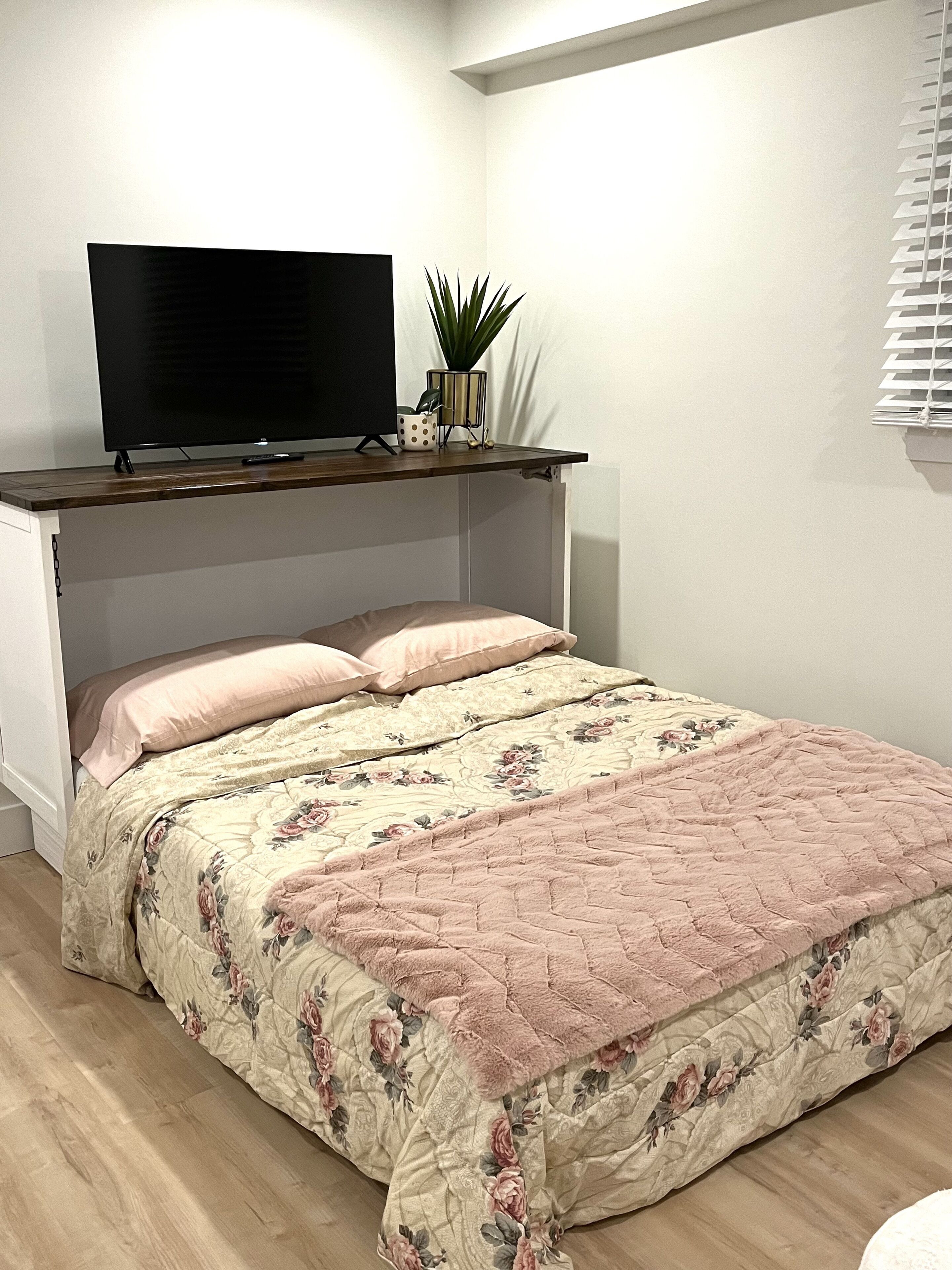 Ein Schlafzimmer mit einem Bett, einem Fernseher auf einem Regal und einer Topfpflanze.