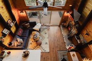 A cozy cabin interior with a wooden floor, a sofa, a coffee table, a fireplace, and a view of the outdoors.