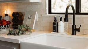 A kitchen with a white countertop, a black faucet, and two soap bottles.