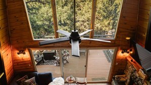 A cozy cabin interior with a large window, wooden floors, a sofa, a coffee table, and a fireplace.