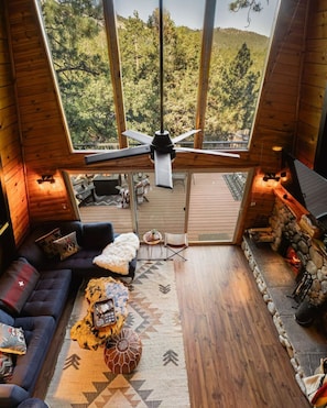 L’intérieur d’un chalet accueillant, avec une grande fenêtre, un plancher en bois, un canapé, une table basse et une cheminée.