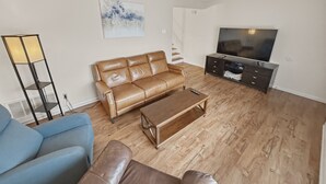 Ein Wohnzimmer mit braunem Ledersofa, einem Couchtisch, einer TV-Konsole und einer Stehlampe.