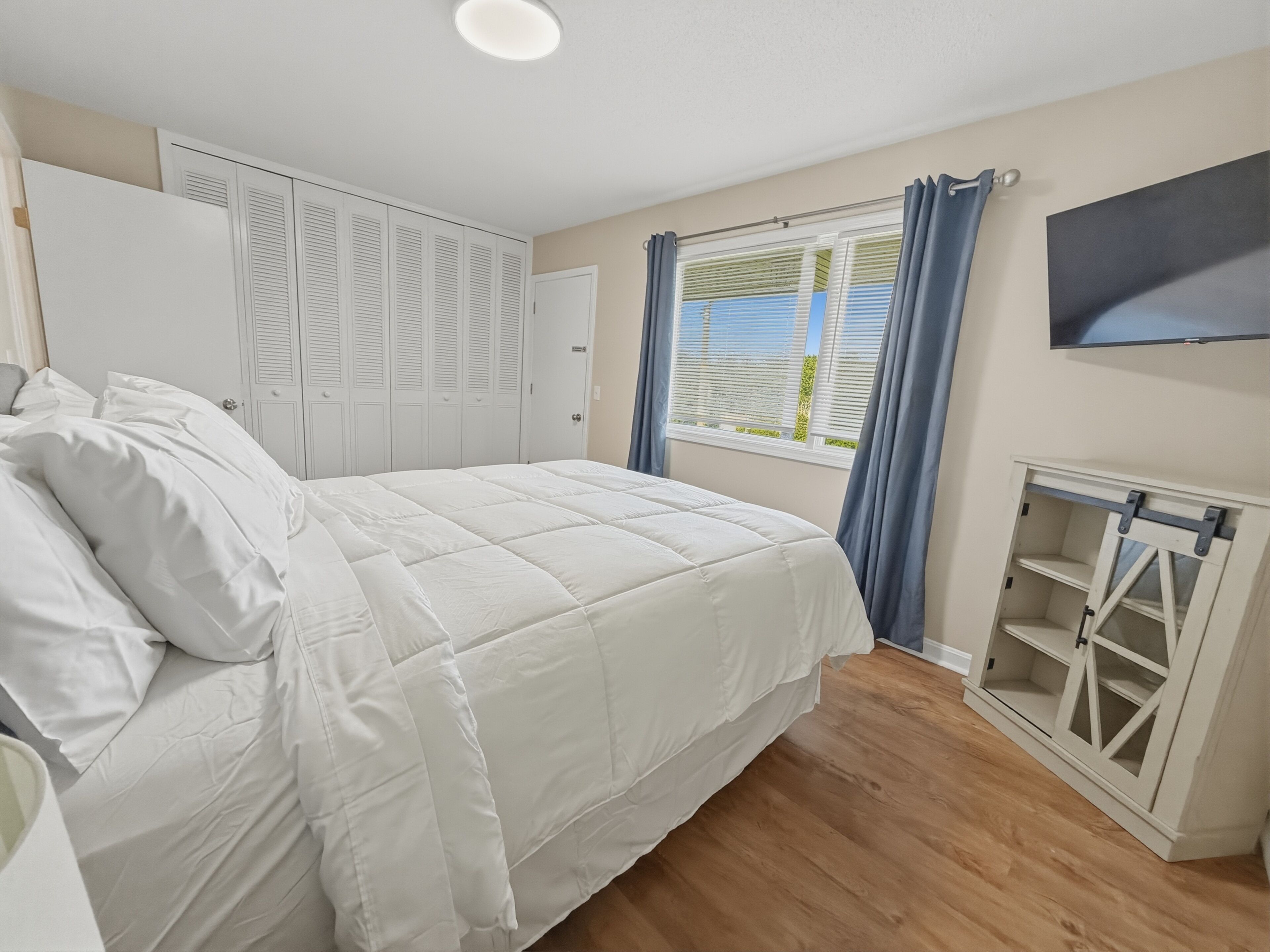 Ein Schlafzimmer mit einem Bett, einem Kleiderschrank, einem Fernseher und einem Fenster mit Vorhängen.