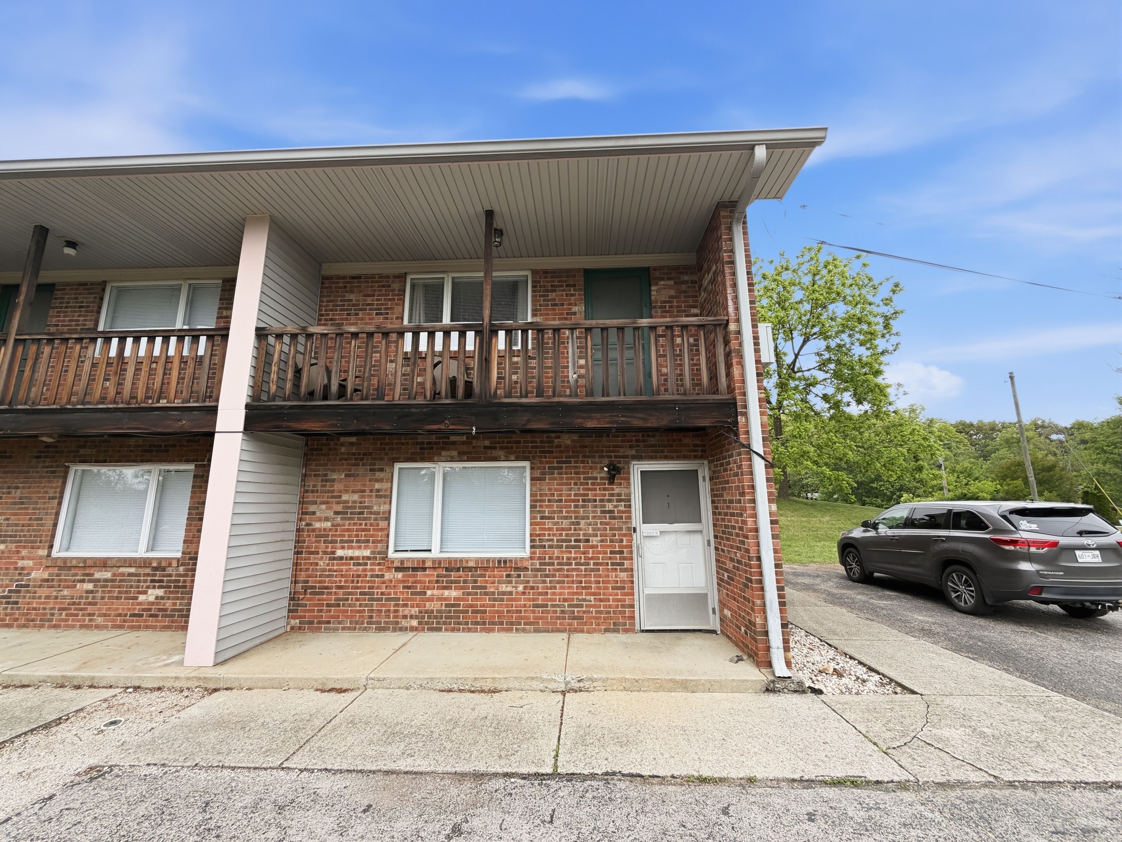 A two-story brick building with a balcony, a garage door, and a parked SUV.