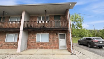 A two-story brick building with a balcony, a garage door, and a parked SUV.