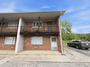 A two-story brick building with a balcony, a garage door, and a parked SUV.