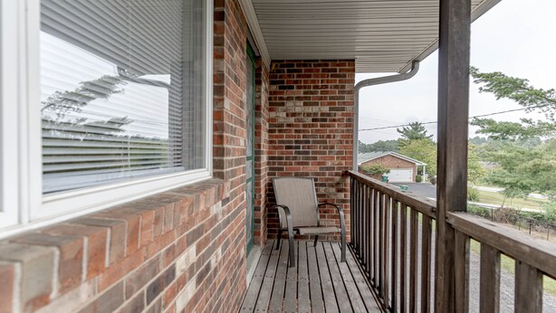 Eine überdachte Veranda mit Backsteinmauer, einem Stuhl und Blick auf eine Wohngegend.
