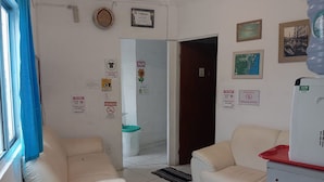 A room with two white sofas, a refrigerator, and a window with blue curtains. There are various signs on the walls, including a 'no smoking' sign and a 'no pets' sign. - Hostel Canários (Palhoça)