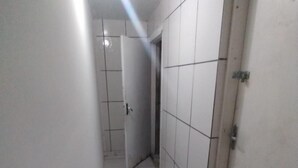 A narrow hallway with white tiled floors and walls, leading to a door marked "SAV". - Hostel Canários (Palhoça)