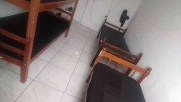 Quarto de dormitório com beliches e uma cama individual. Há uma porta, uma televisão presa à parede e uma pequena mesa com uma cadeira.