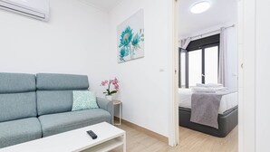 A modern room with a grey sofa, a white coffee table, a small side table with a potted orchid, and a bed with a grey blanket. - Nueva I - holiday rental in Nerja (Nerja)