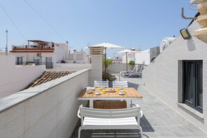 Une terrasse sur le toit, avec une table en bois, des chaises blanches et des parasols.