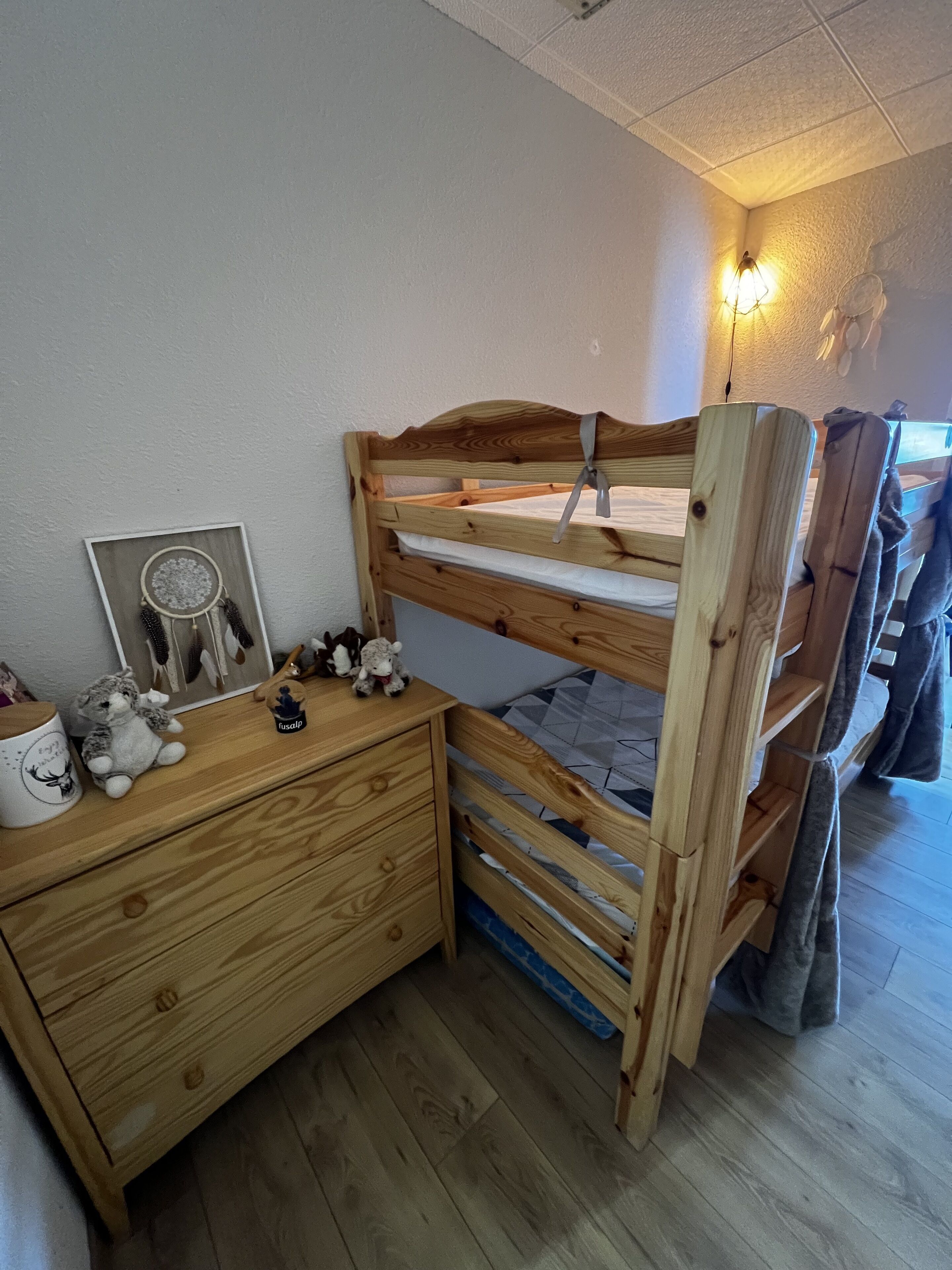 A bunk bed with a wooden headboard, a nightstand with a drawer, a framed dreamcatcher, and a small stuffed animal.
