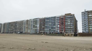 Een meerlaags woongebouw met een gelijke gevel, een zichtbare trap naar de ingang en zandgrond ervoor.