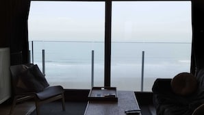Een kamer met uitzicht op zee, een bank, een stoel en een tafeltje.