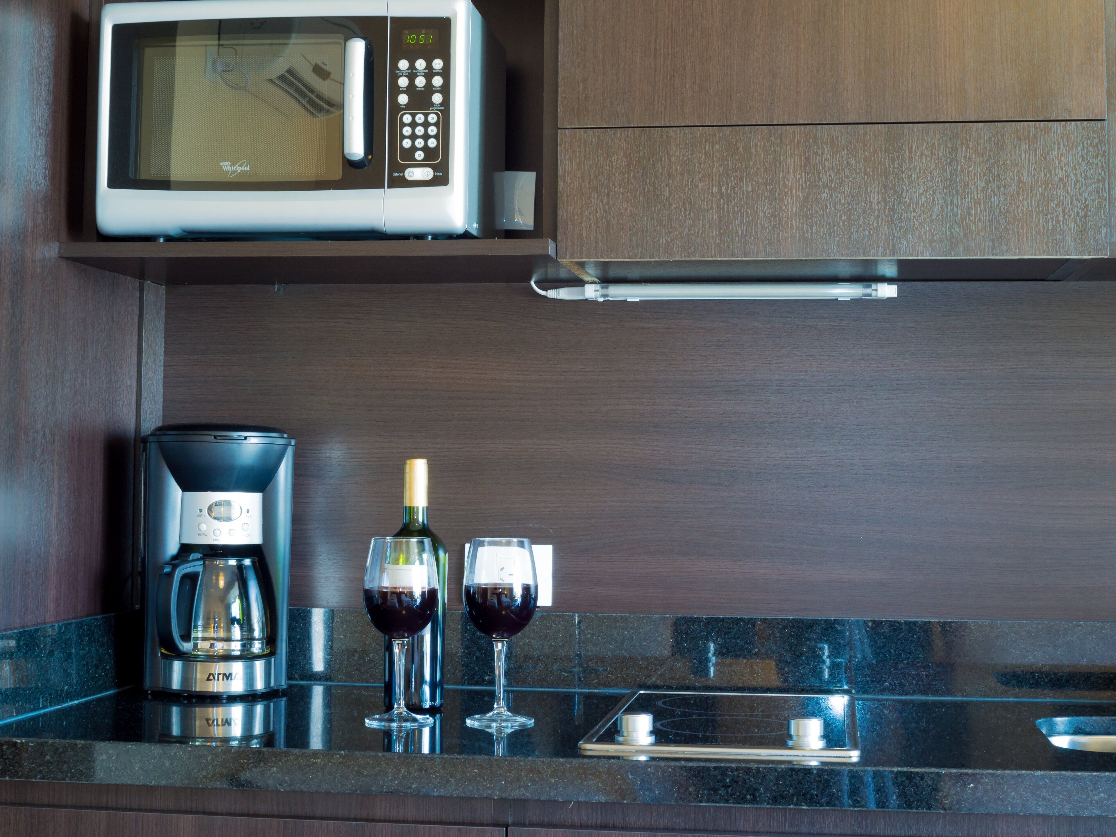 Une cuisine équipée d’un four à micro-ondes, d’une machine à café et de deux verres à vin posés sur le comptoir.