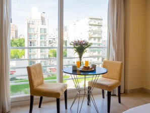 Een kamer met twee stoelen, een tafel met een bloevas, en een raam met uitzicht op de stad.