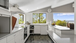 A modern kitchen with white cabinets, a built-in oven, and a large window offering a view of greenery and the sea. - Ngaio Views - Lake Taupo Holiday Home (Taupo)