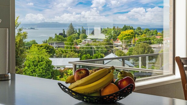 A view from a balcony with a fruit bowl on the table, overlooking a cityscape and a body of water. - Ngaio Views - Lake Taupo Holiday Home (Taupo)