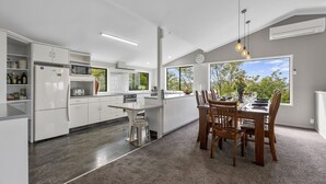 A modern kitchen with white cabinetry, a central island, and a dining area with wooden chairs and a table. - Ngaio Views - Lake Taupo Holiday Home (Taupo)