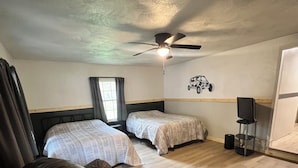 Une chambre avec deux lits, un ventilateur de plafond, une télévision et une fenêtre avec des rideaux.