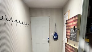 Un couloir avec une porte blanche, un sac bleu accroché au mur et un plancher en bois.
