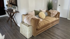 Ein gemütliches Wohnzimmer mit einem braunen Sofa, einem kleinen Tisch mit Dekoration und einer großen Pflanze.