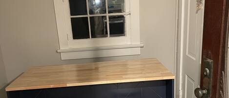 Un coin cuisine avec un plan de travail en bois, deux tabourets, une fenêtre et une porte.