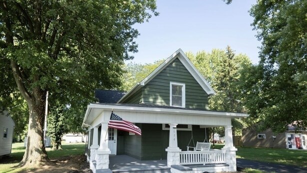 Ein grünes Haus mit weißem Veranda und einer amerikanischen Flagge.