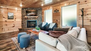 Un salon chaleureux avec des murs en bois, une cheminée en pierre, un canapé, des poufs et une table basse.