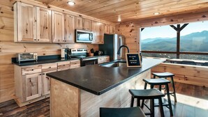 Une cuisine rustique, située dans une cabane en bois, avec un grand îlot central, des armoires en bois, un four à micro-ondes et un réfrigérateur.