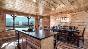 L’intérieur d’un chalet en bois comprend une cuisine, un coin repas et de grandes fenêtres offrant une vue sur les montagnes.