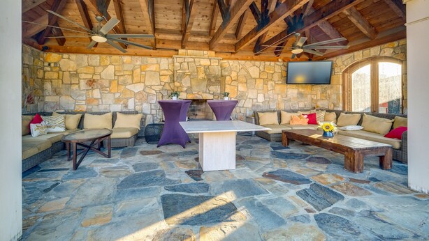 Un patio al aire libre con suelo de piedra, vigas de madera y mobiliario que incluye sofás y mesas.