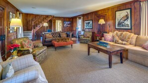 Un salón amplio con una imponente escalera, asientos cómodos y una chimenea.