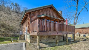 Une cabane en rondins avec une terrasse en bois, des fondations en pierre et un ciel bleu clair en arrière-plan.