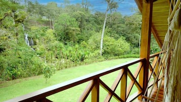 A wooden deck with a view of a lush garden and a waterfall.
