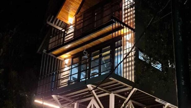 Een modern huis met een houten gevel en een balkon, omgeven door groen.