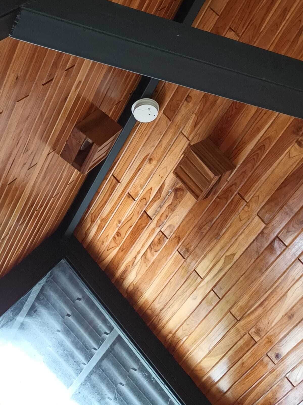 A wooden ceiling with a black beam and a white smoke detector.