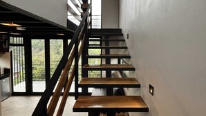 Een moderne trap met houten treden en zwarte leuningen, leidend naar een balkon met uitzicht op groen.