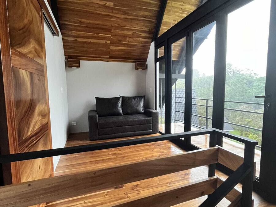 A modern interior with a wooden ceiling, a black leather sofa, and large windows offering a view of the outdoors.