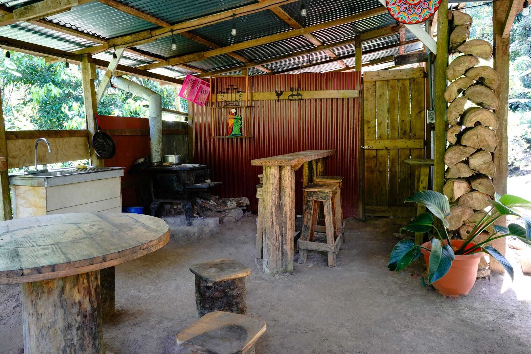 Een rustieke buitenkeuken met een spoelbak, houten krukken en een tafel.