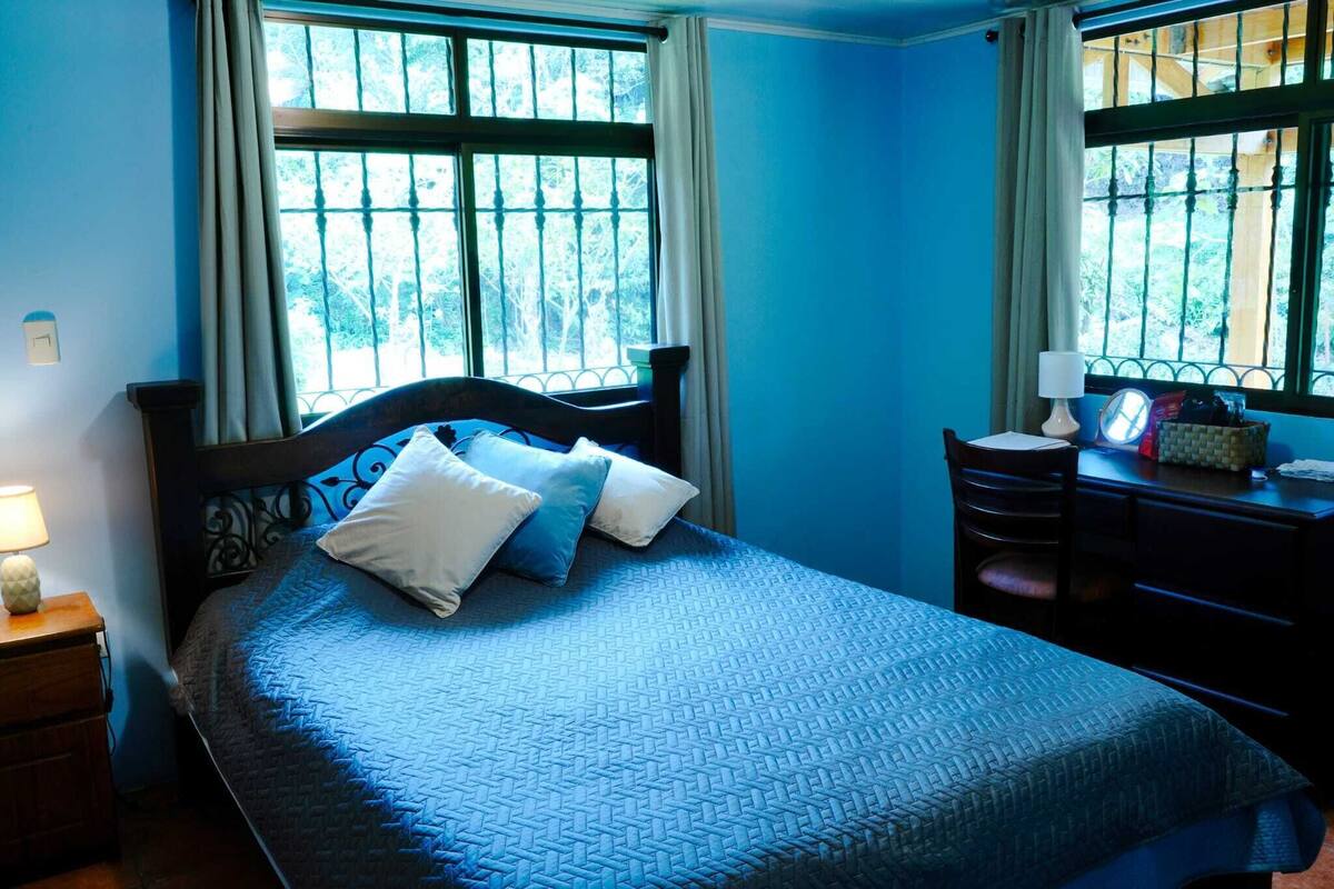 Ein Schlafzimmer mit einem Bett, einem Schreibtisch und zwei Fenstern mit Vorhängen.