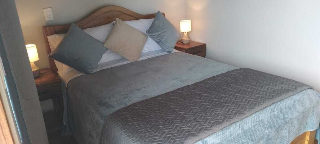 A neatly made bed with a grey blanket and pillows, a wooden headboard, and bedside lamps on wooden nightstands.