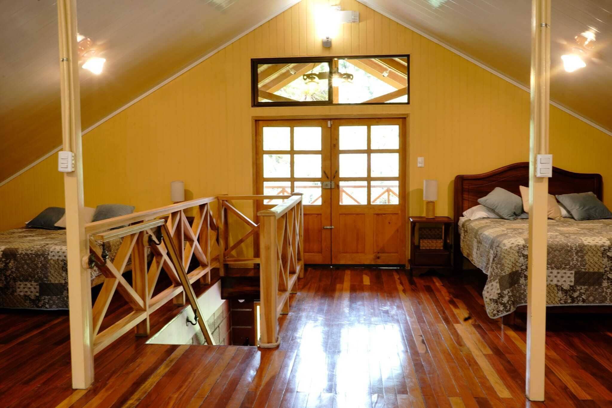 A cozy attic bedroom with a wooden staircase, a large window, and a bed with a quilt.